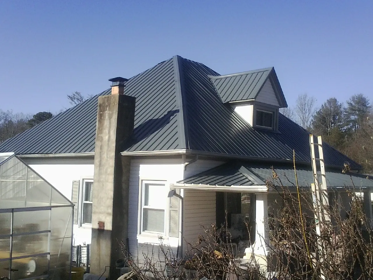 Dark blue standing seam metal roof on a white farmhouse with dormer — Slate & Tile Roof Repair by Roofing Brothers in Fallston