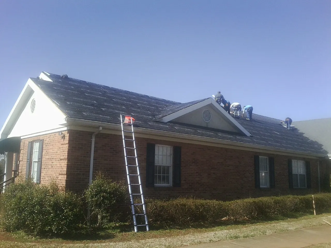 Crew tearing shingles off a brick ranch roof with a ladder set — Metal Roof Repair work by our crew in Fallston