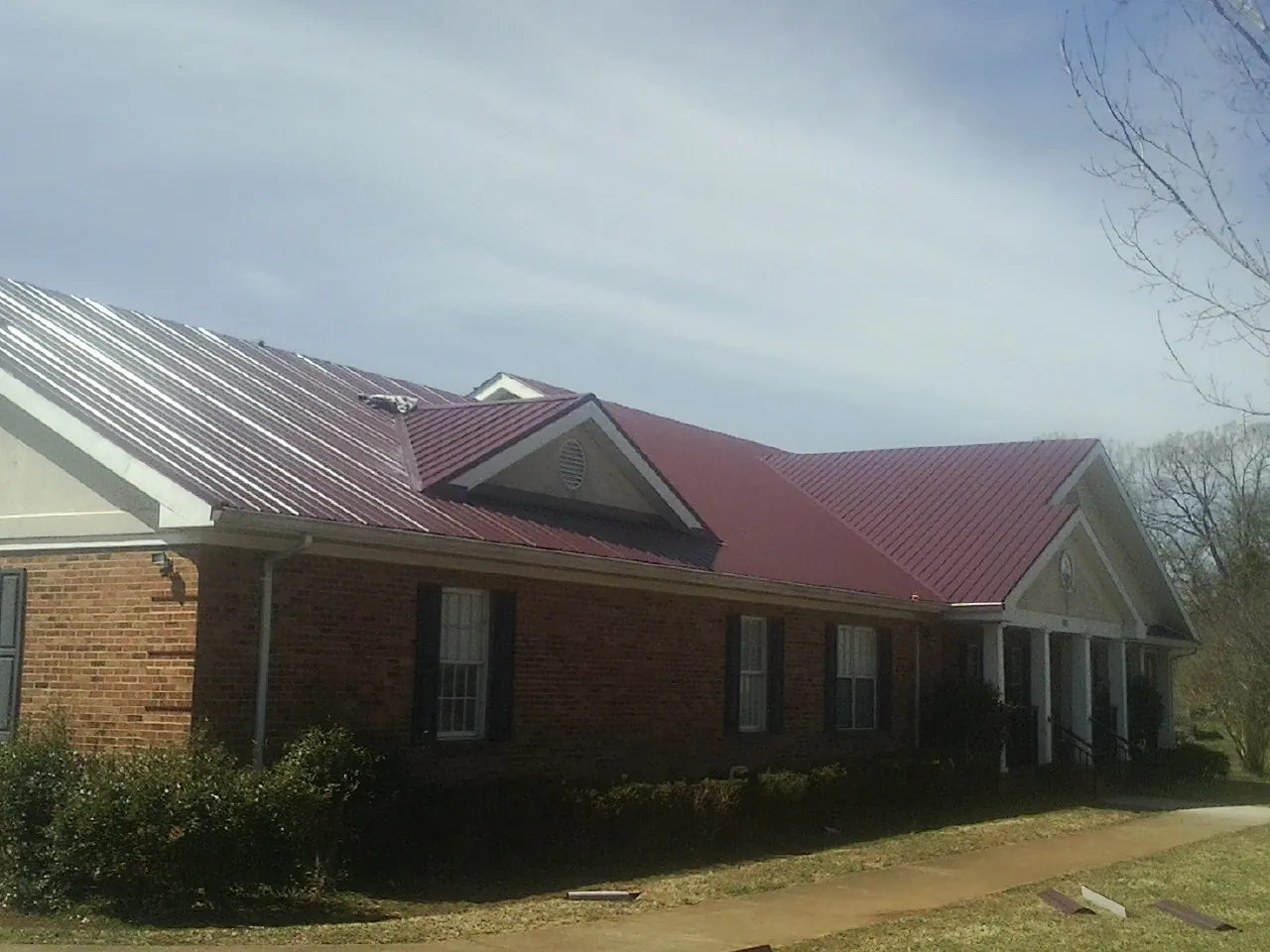 Red metal roof with gabled entries on a long brick building, from a Hail Damage Roof Repair job in Fallston